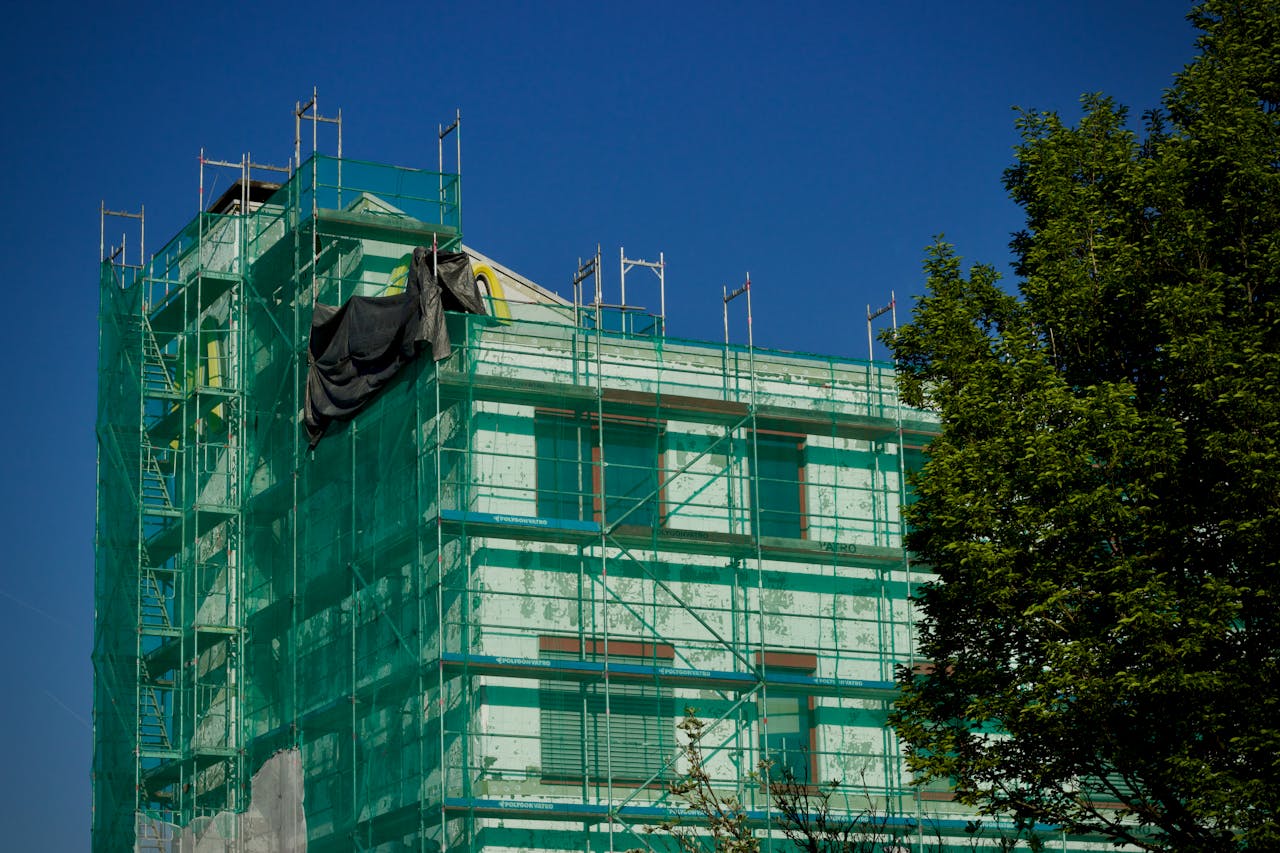 Building under renovation covered with green scaffolding against a clear blue sky.